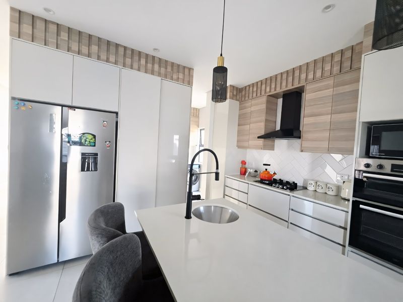 Modern kitchen featuring sleek white and wood-grain cabinetry, a central island with a prep sink, integrated appliances, and a stylish tiled backsplash.