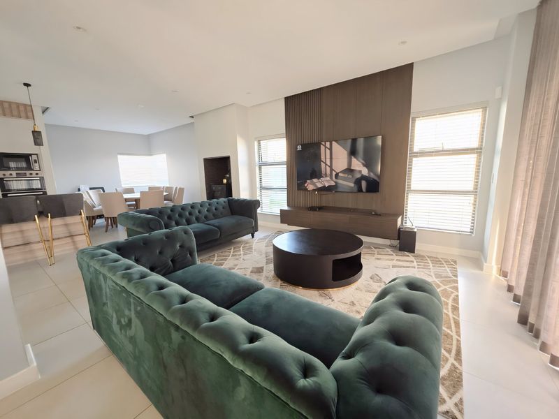 Spacious open-plan living and dining area featuring modern tiled floors, a stylish feature wall with integrated media unit, and contemporary kitchen finishes.