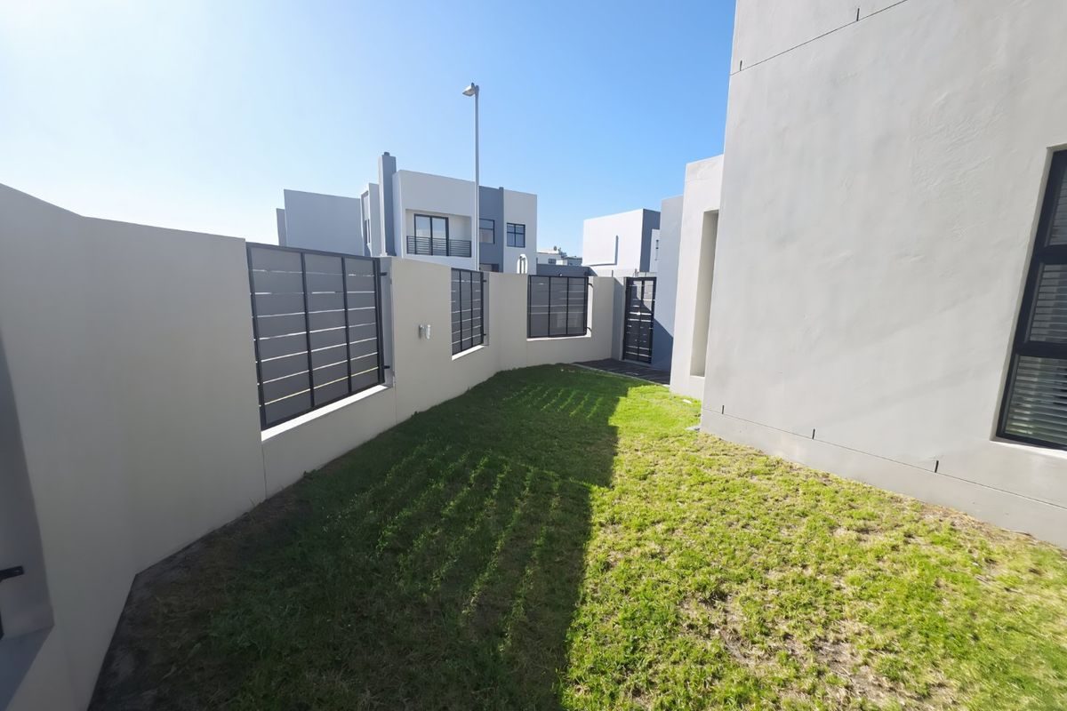 A private rear garden area featuring a well-maintained lawn, enclosed by modern boundary walls with integrated metal slat fencing and a secure pedestrian gate.