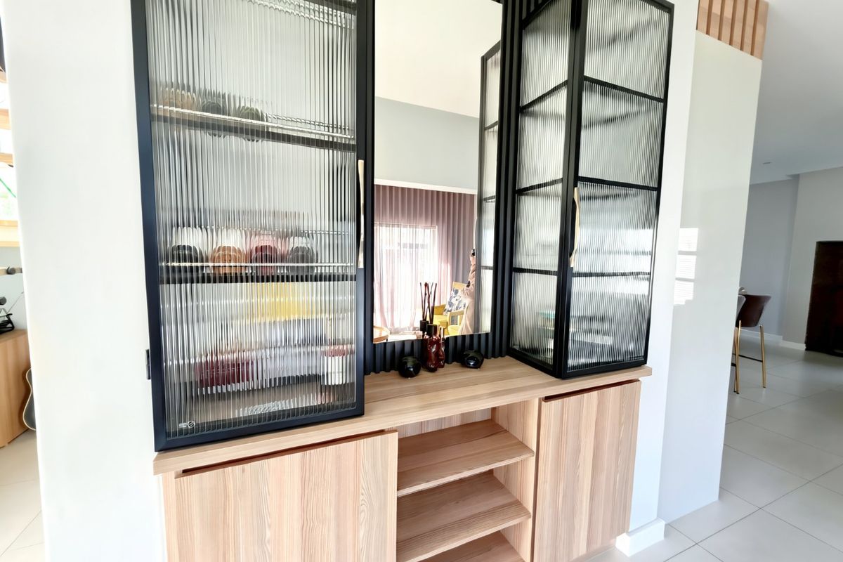 Modern built-in cabinetry featuring fluted glass display doors, integrated mirror, and stylish slatted timber wall paneling in a bright living space.