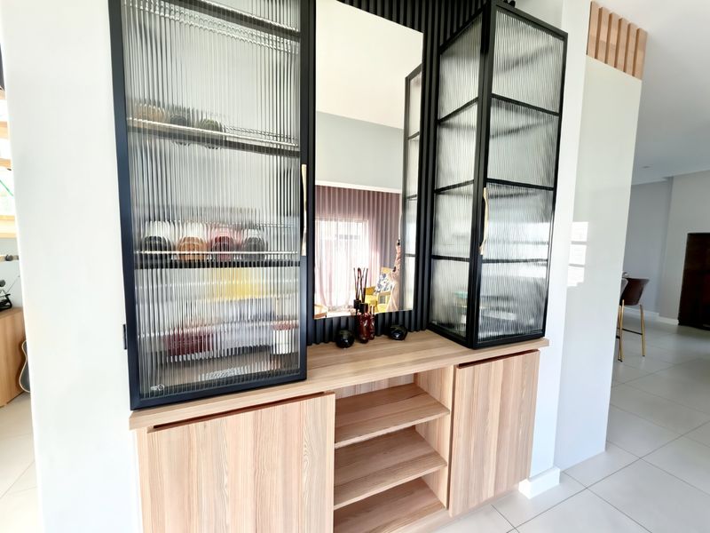 Modern built-in cabinetry featuring fluted glass display doors, integrated mirror, and stylish slatted timber wall paneling in a bright living space.
