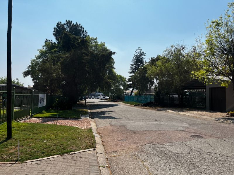 A street-level view of the commercial property frontage, featuring paved access roads, established landscaping, and secure perimeter fencing.