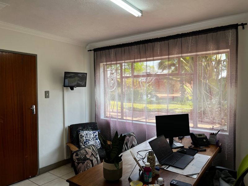 A functional office space featuring tiled flooring, large window with natural light, and standard overhead lighting.