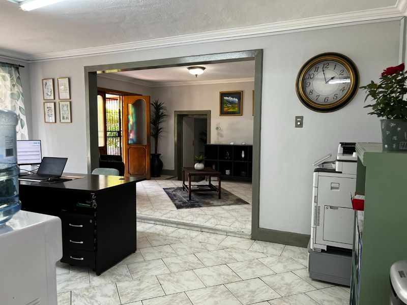 A functional commercial office space featuring tiled flooring, neutral walls, and an open-plan layout connecting to an adjacent reception or waiting area.