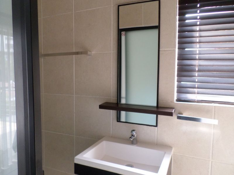 A modern bathroom featuring a wall-mounted basin with a mixer tap, tiled walls, a mirror with a shelf, and venetian blinds.