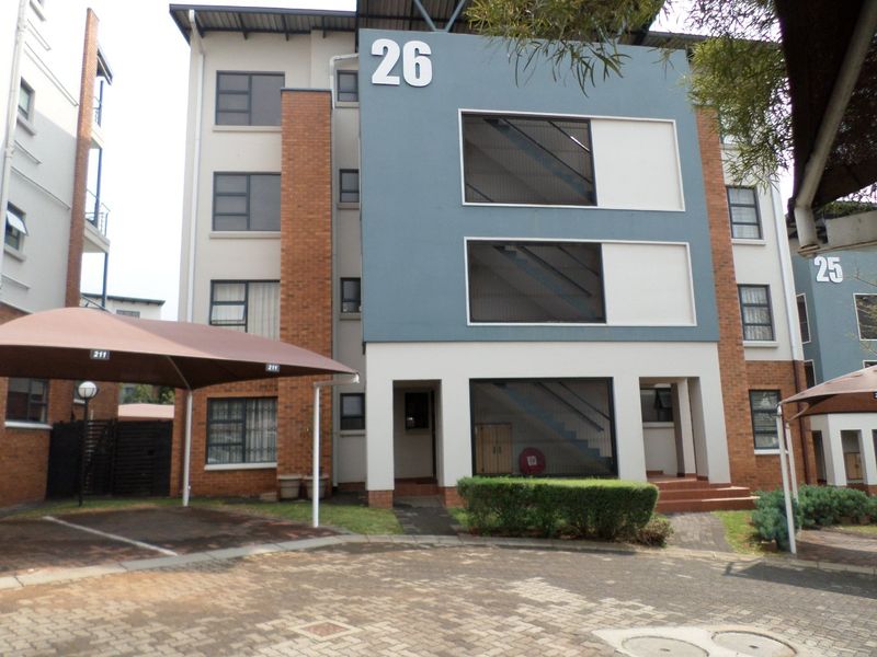 Front elevation of a multi-story apartment building featuring brick and painted facade, aluminum windows, and an adjacent covered carport area.