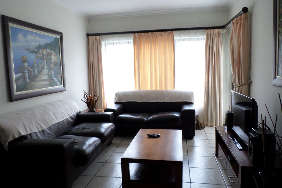 A comfortable living room featuring neutral tiled flooring and large windows with curtain rails, providing a bright and functional space.