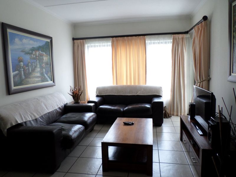 A comfortable living room featuring neutral tiled flooring and large windows with curtain rails, providing a bright and functional space.