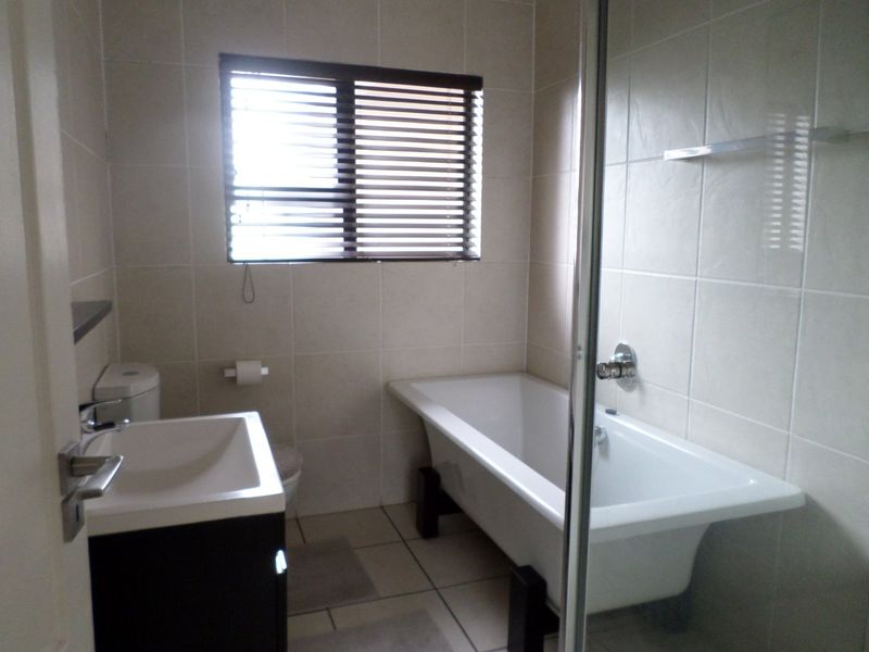 A functional bathroom featuring a freestanding bathtub, vanity basin, toilet, and a glass-enclosed shower area with neutral wall and floor tiling.