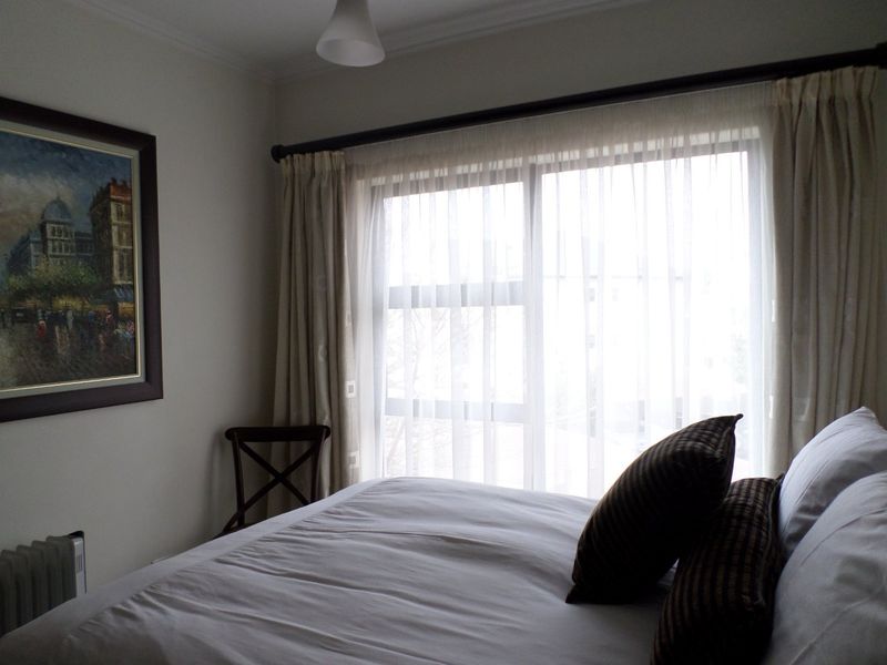 A cozy bedroom featuring a large sliding glass door with curtains, a wall-mounted radiator, and neutral wall finishes.