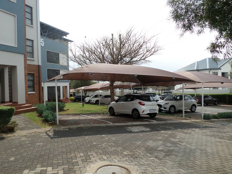 Exterior view of the apartment complex featuring paved parking areas with dedicated shade cloth carports and established garden landscaping.