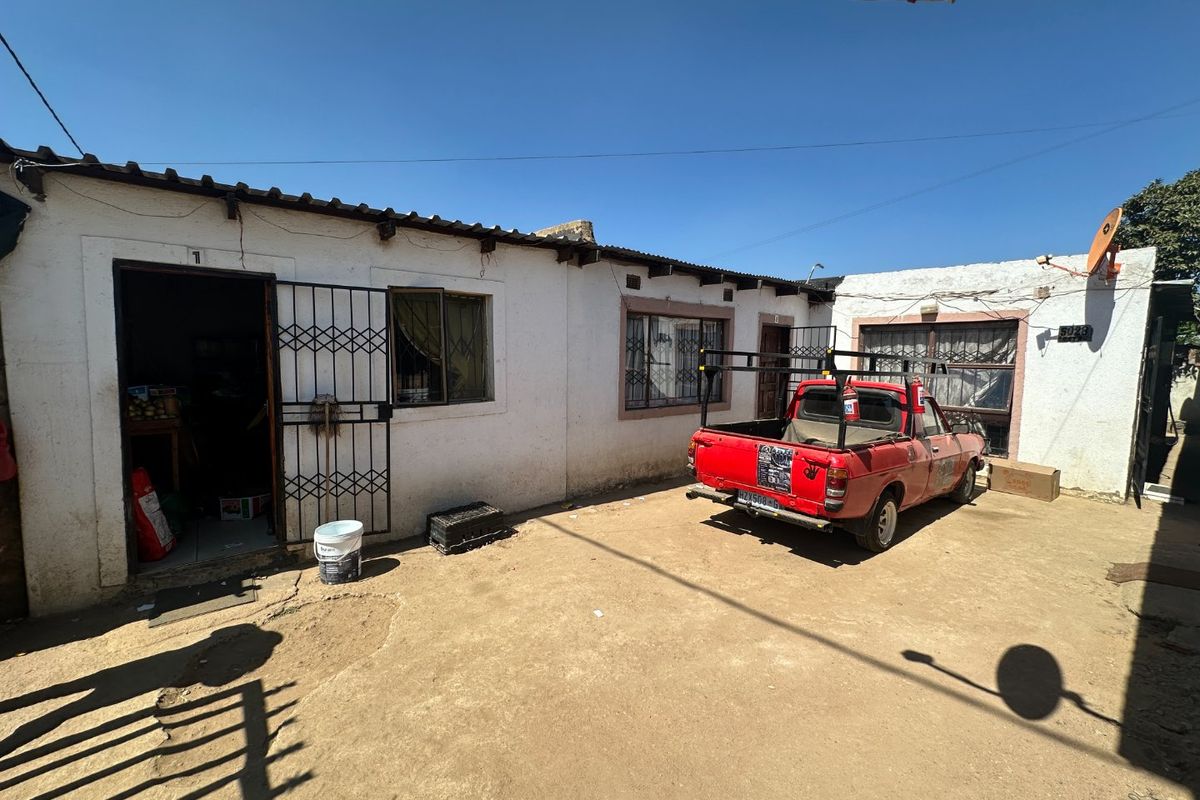 Rear exterior view of the property featuring a dirt courtyard, security gates, and basic building structure with a tiled roof.