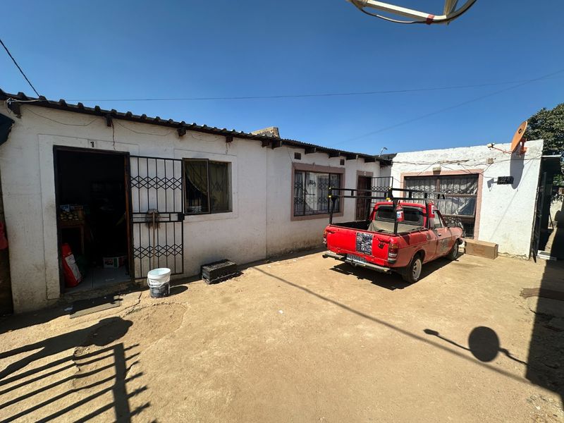 Rear exterior view of the property featuring a dirt courtyard, security gates, and basic building structure with a tiled roof.