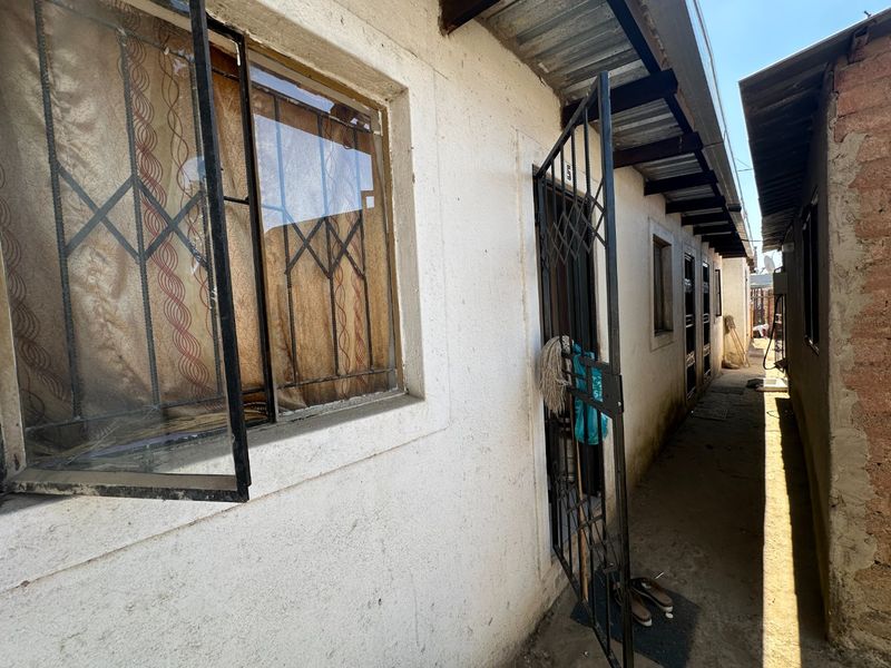 A narrow exterior side passage featuring concrete flooring, metal security gates, and window frames along the side of the residential structure.