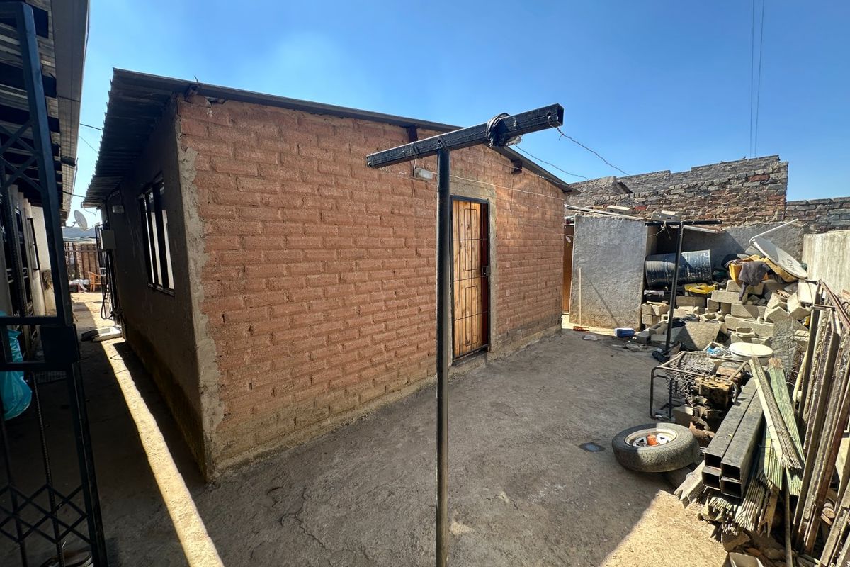 Rear exterior view of a brick structure featuring a metal security door and a concrete yard area with utility space.