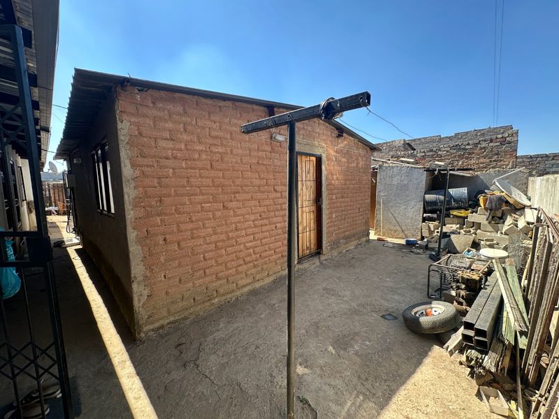 Rear exterior view of a brick structure featuring a metal security door and a concrete yard area with utility space.