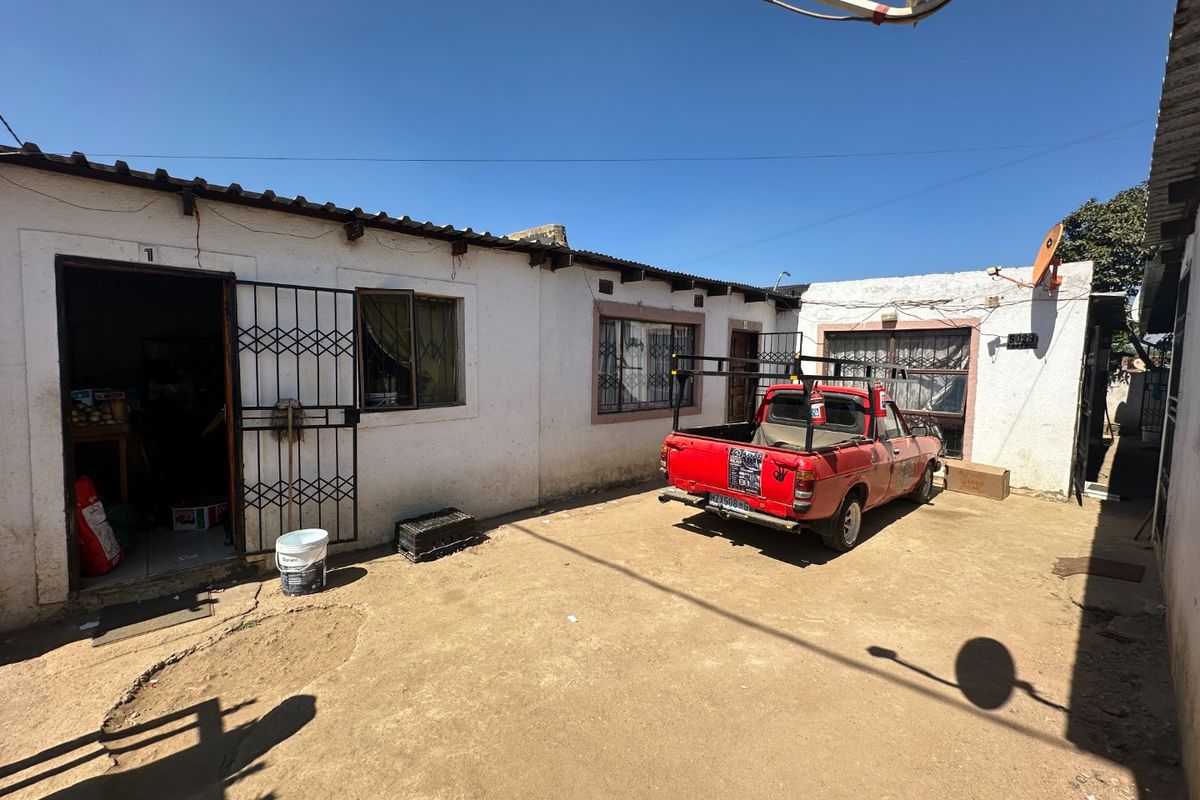 Rear exterior view of the property featuring a concrete yard, security gates, and burglar bars on the windows.