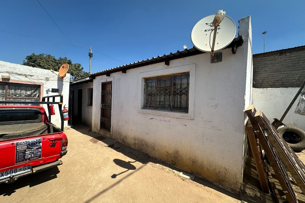 Rear exterior view of the property showing a single-story structure with metal security features and visible wear to the exterior wall finishes.