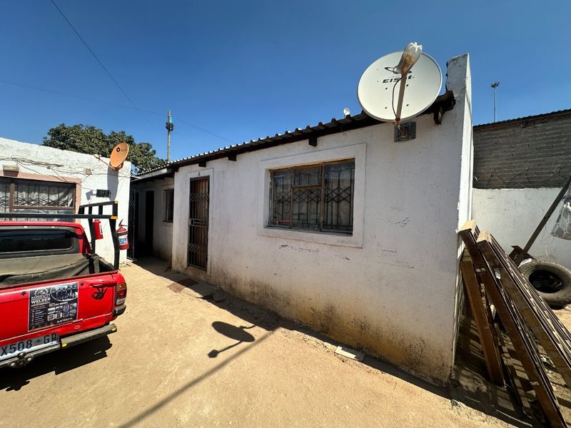 Rear exterior view of the property showing a single-story structure with metal security features and visible wear to the exterior wall finishes.