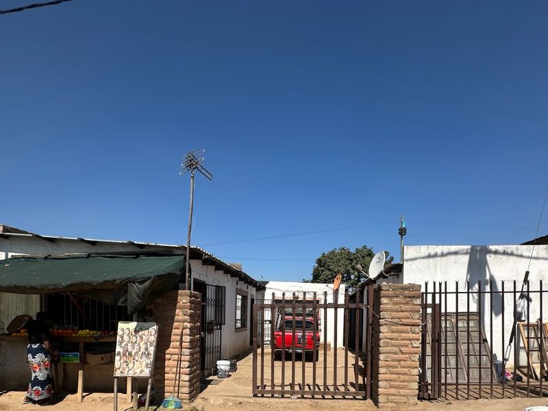 Front view of the property featuring a brick perimeter wall, metal security gate, and an unpaved driveway area.