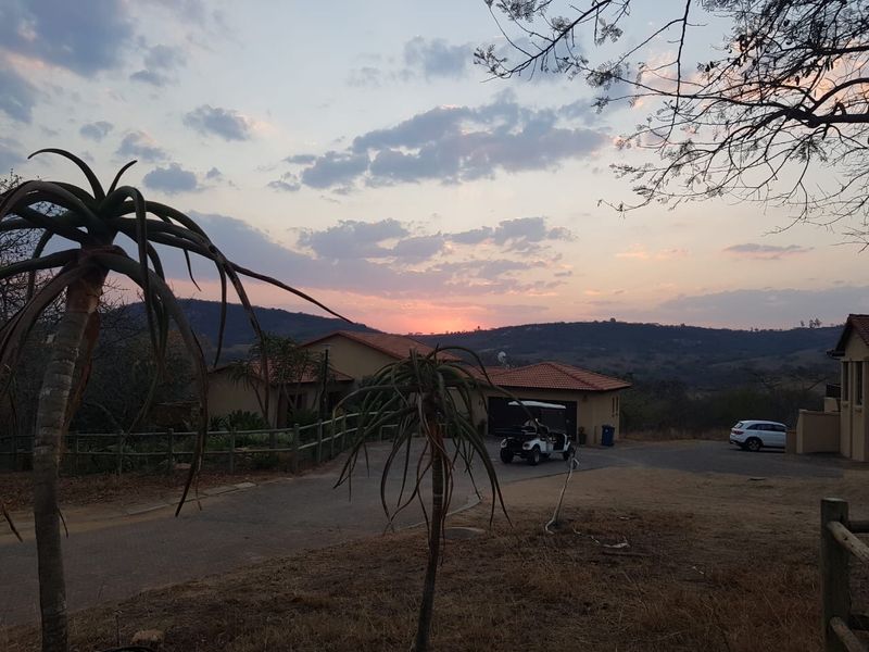 A scenic view of a residential property exterior featuring a paved driveway, garage, and timber fencing set against a sunset landscape.