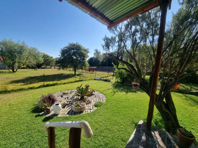 A covered patio area overlooking a well-maintained garden with a circular stone feature and mature trees.