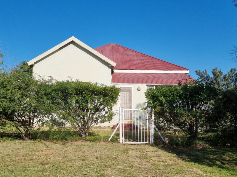 Front elevation of a single-story house featuring a red corrugated metal roof and a gated entrance with security screen door.