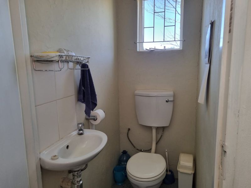 A compact guest bathroom featuring a wall-mounted basin, toilet, and a small window with security bars.