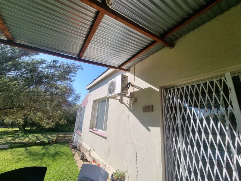 Covered patio area featuring a corrugated metal roof, security gate access, and an exterior wall-mounted air conditioning unit overlooking the garden.