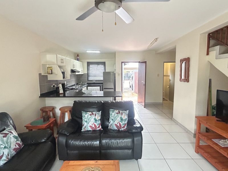 Open-plan living area featuring a kitchen with granite countertops, tiled flooring, and a staircase leading to the upper level.
