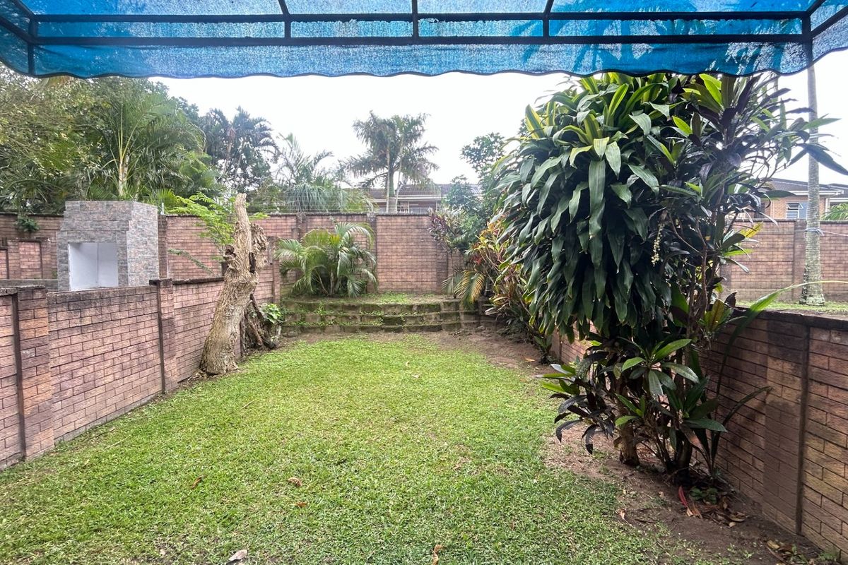 A private rear garden featuring a lawn, brick boundary walls, and a built-in braai area under a blue shade cloth awning.