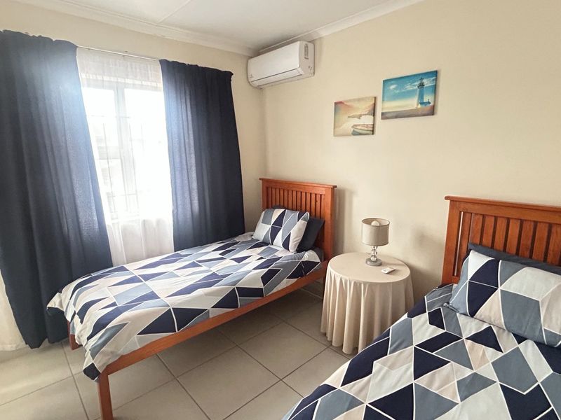 A functional bedroom featuring tiled flooring, a wall-mounted split-system air conditioner, and neutral wall finishes.