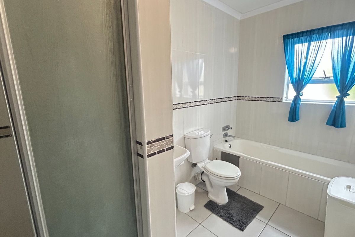 A functional bathroom featuring a bathtub, separate shower enclosure, and tiled finishes throughout, offering a clean and practical layout.