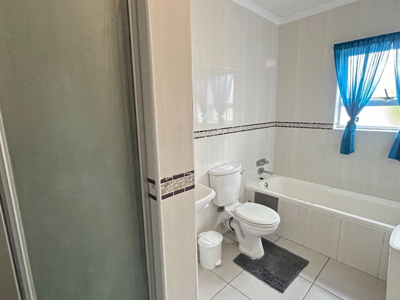 A functional bathroom featuring a bathtub, separate shower enclosure, and tiled finishes throughout, offering a clean and practical layout.