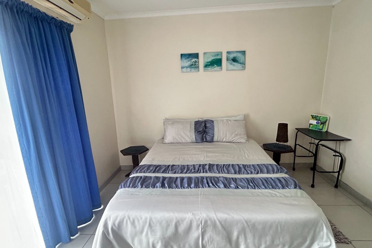 A functional bedroom featuring tiled flooring, an integrated air conditioning unit, and access to a balcony via a sliding door.