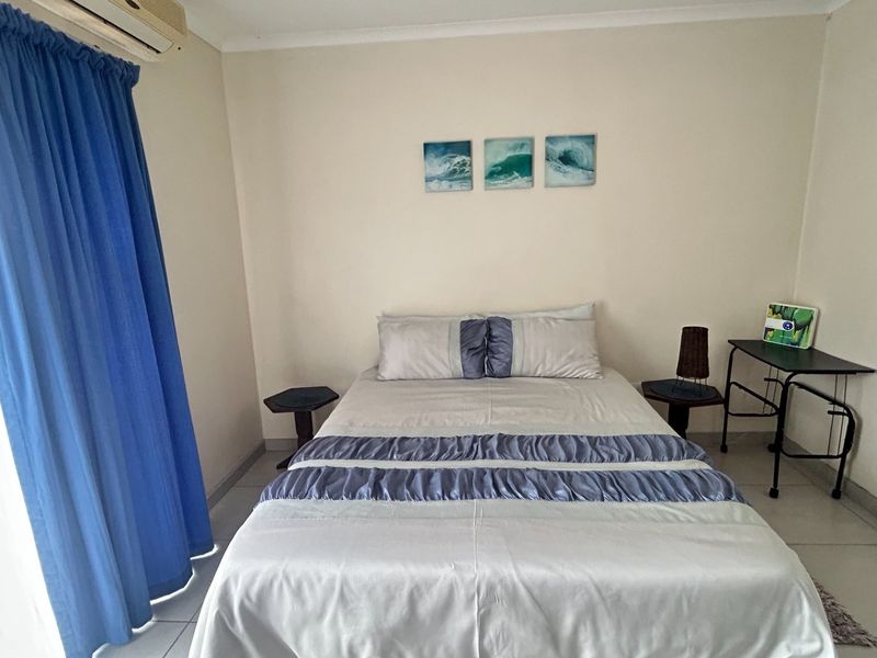 A functional bedroom featuring tiled flooring, an integrated air conditioning unit, and access to a balcony via a sliding door.