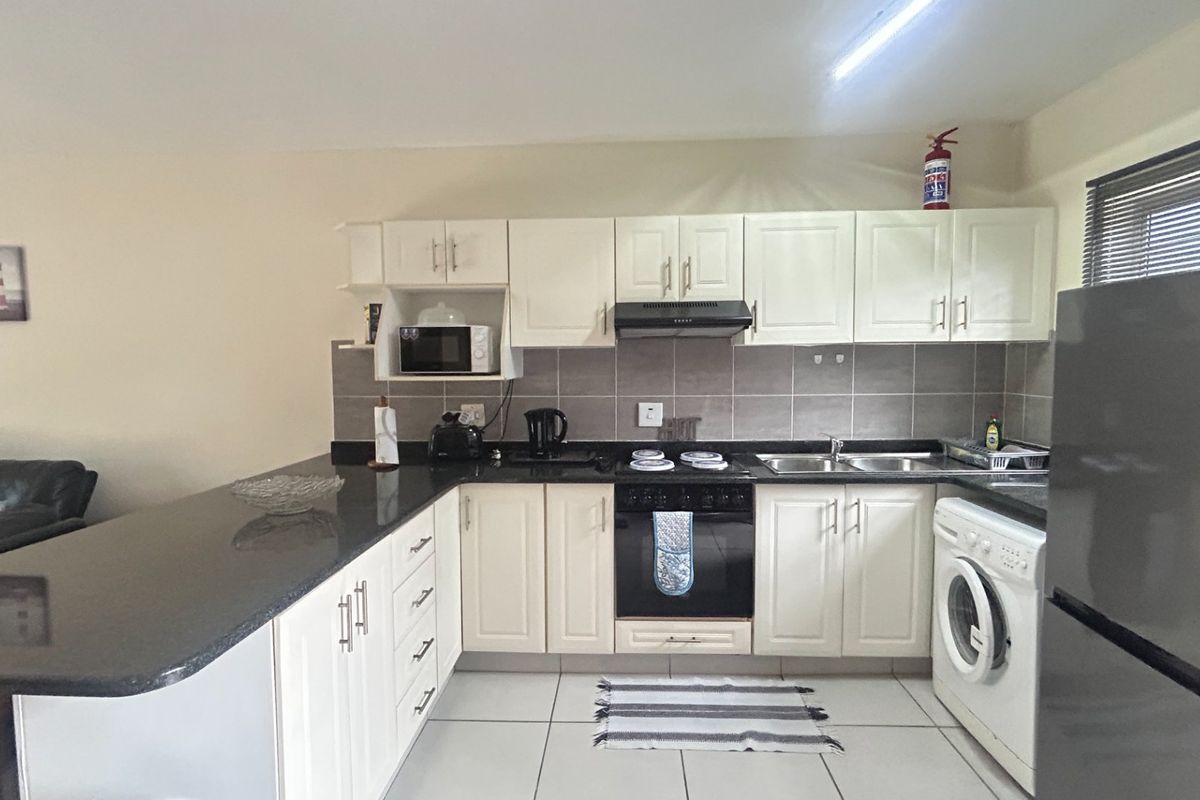 A functional kitchen featuring white cabinetry, dark granite countertops, tiled backsplash, and integrated appliances including an oven, hob, and extractor fan.