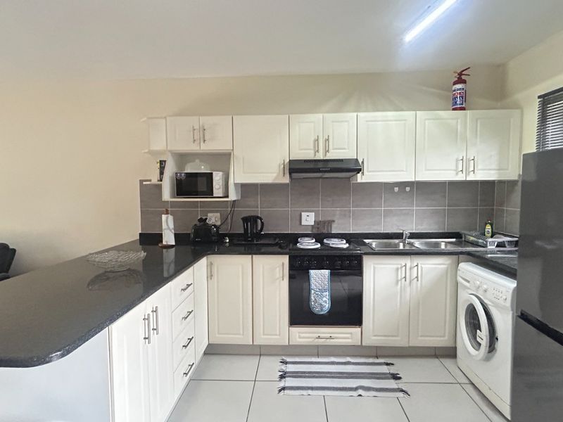 A functional kitchen featuring white cabinetry, dark granite countertops, tiled backsplash, and integrated appliances including an oven, hob, and extractor fan.