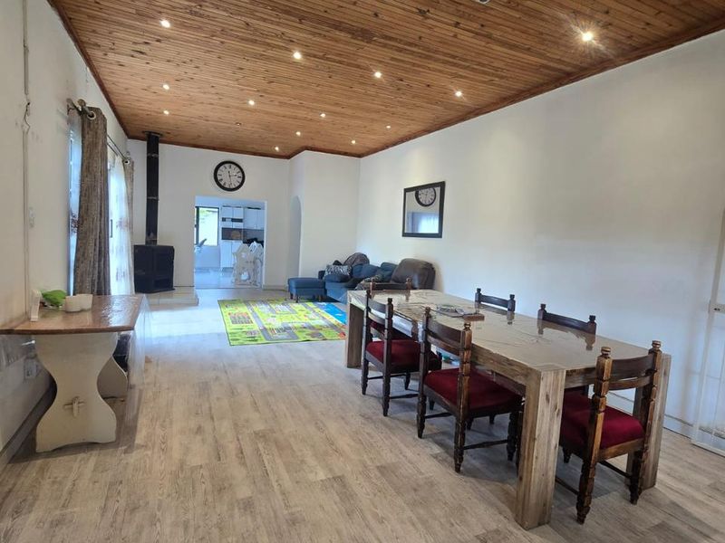 Spacious open-plan living and dining area featuring a distinctive wood-paneled ceiling, recessed lighting, and a cozy wood-burning fireplace.
