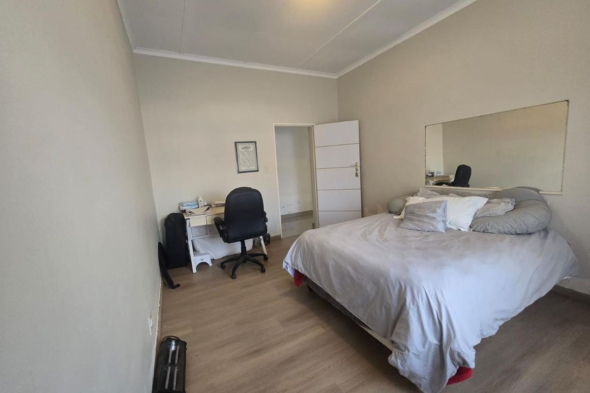 A functional bedroom featuring light-toned laminate flooring, a large wall-mounted mirror, and neutral wall finishes.