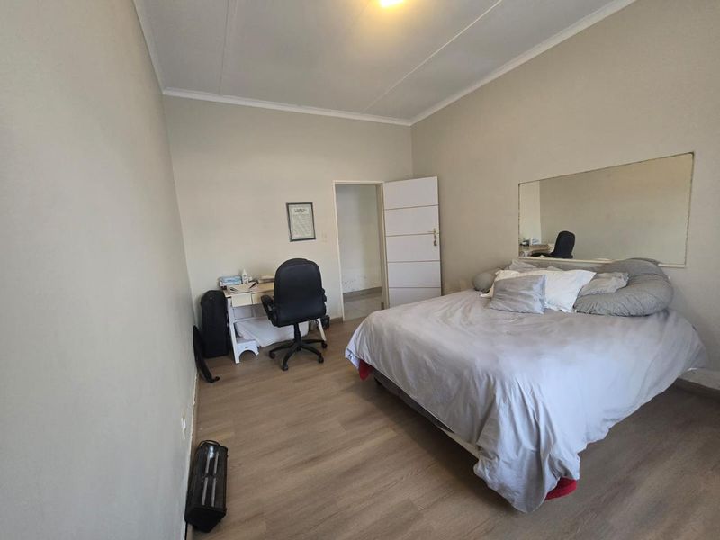 A functional bedroom featuring light-toned laminate flooring, a large wall-mounted mirror, and neutral wall finishes.