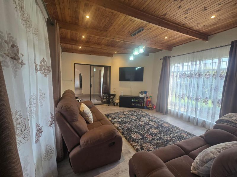 A comfortable living room featuring a warm timber tongue and groove ceiling, recessed lighting, and large windows that provide ample natural light.