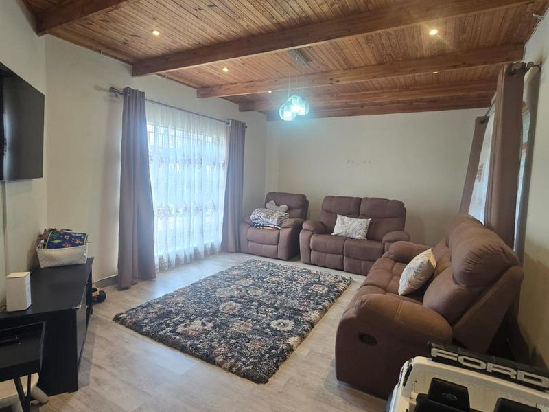 A living room featuring a vaulted timber-clad ceiling with exposed beams, recessed lighting, and light-toned laminate flooring.
