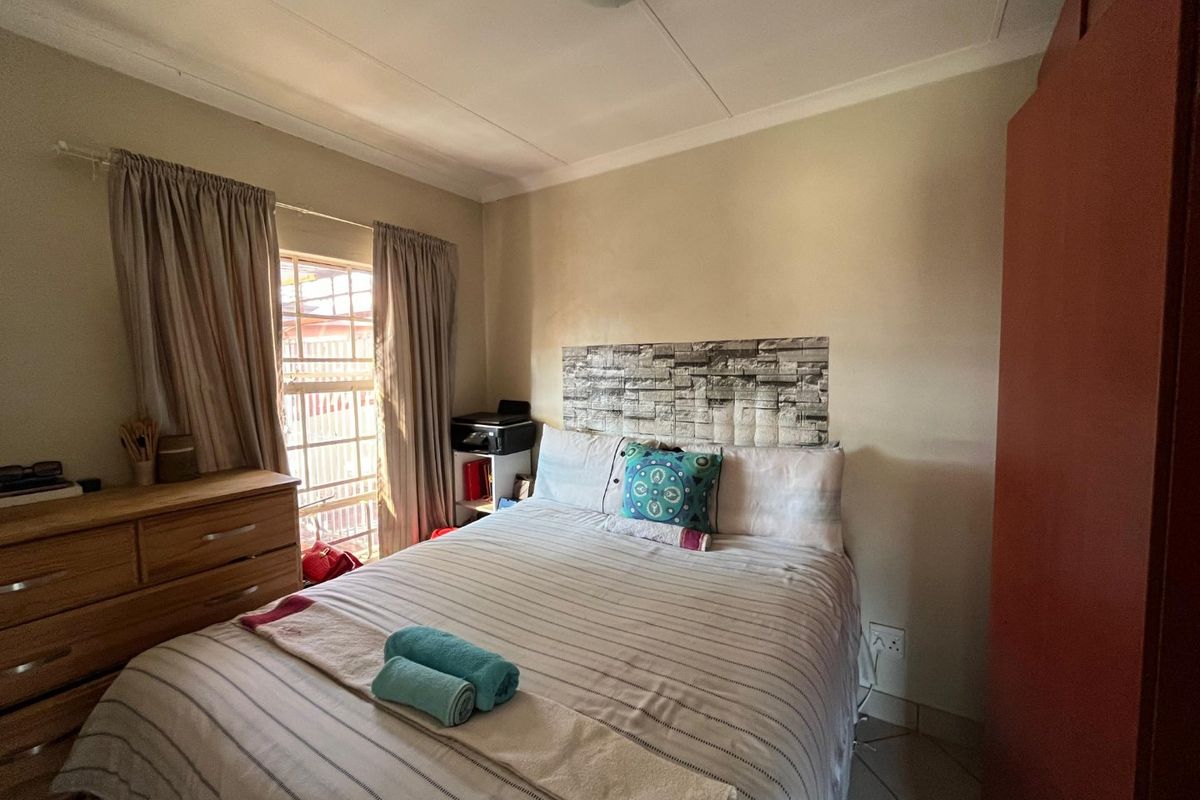 A functional bedroom featuring tiled flooring, a window with security bars, and neutral wall finishes.