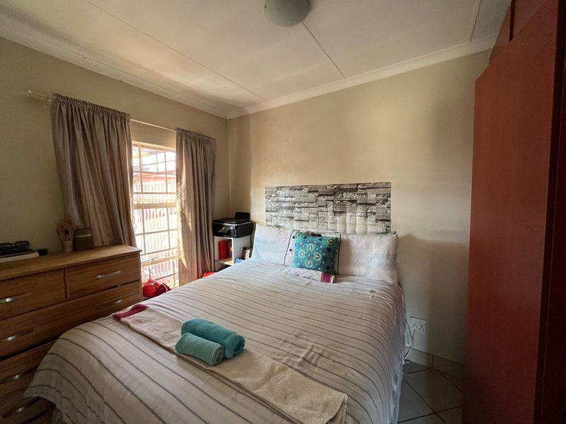 A functional bedroom featuring tiled flooring, a window with security bars, and neutral wall finishes.