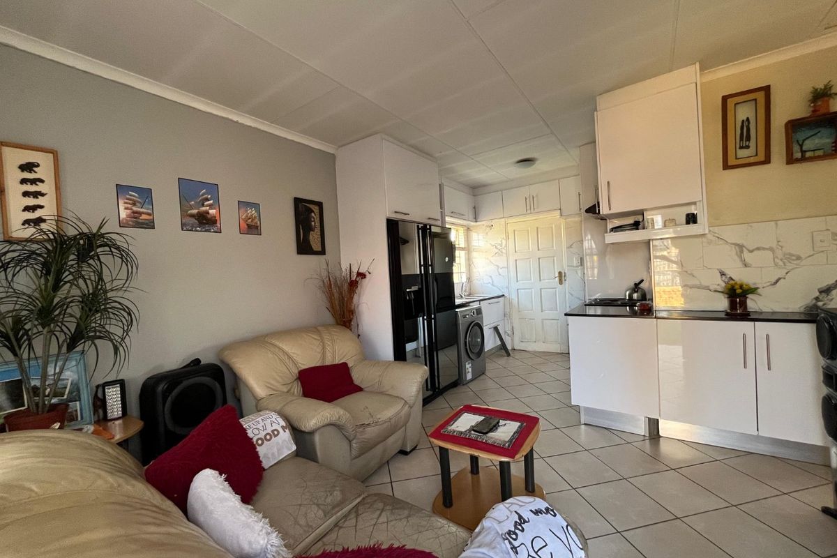 Open-plan living area featuring a compact kitchen with modern white cabinetry, marble-look splashback, and tiled flooring throughout.