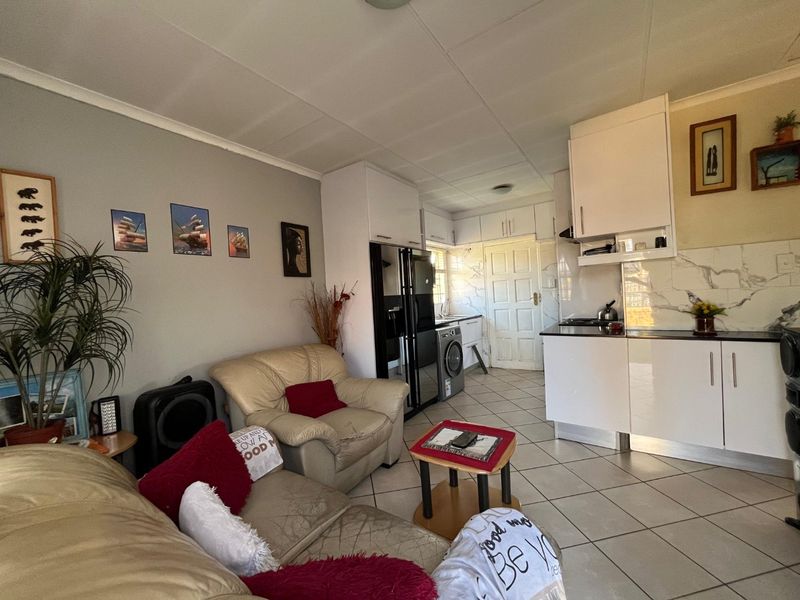 Open-plan living area featuring a compact kitchen with modern white cabinetry, marble-look splashback, and tiled flooring throughout.