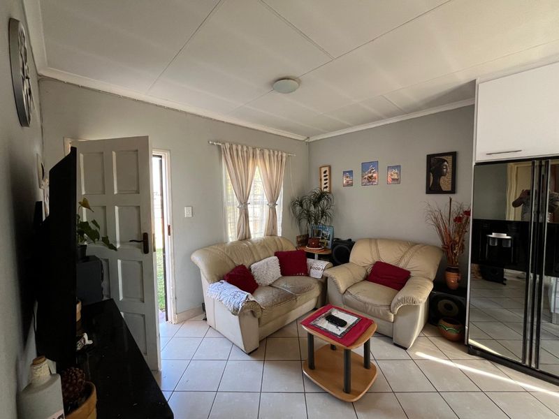 A compact living area featuring tiled flooring and a panelled ceiling, with direct access to the exterior through a side door.