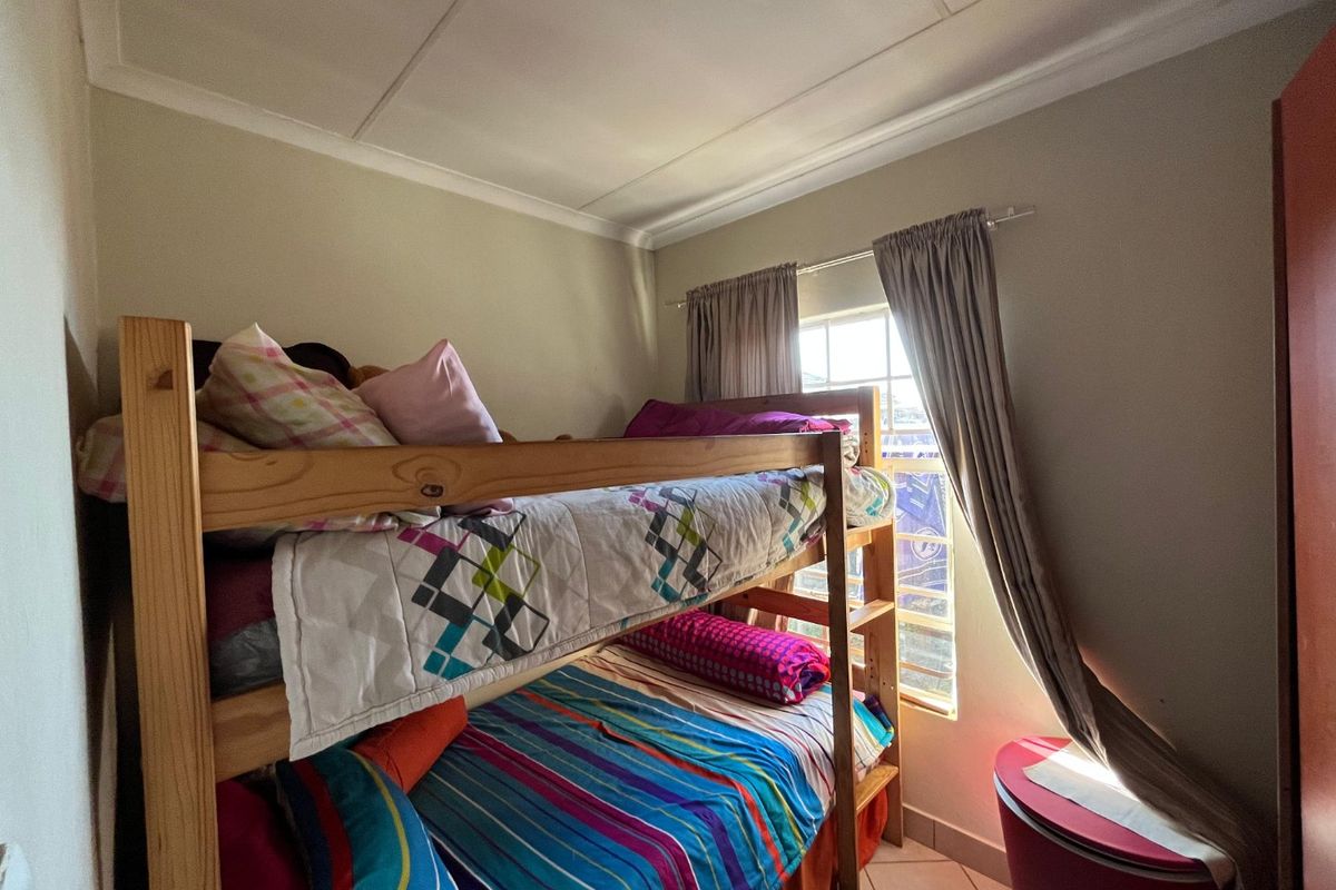 A functional bedroom featuring tiled flooring, ceiling cornicing, and a window with curtain tracks.
