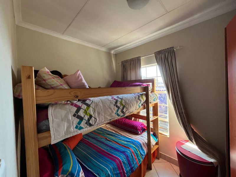 A functional bedroom featuring tiled flooring, ceiling cornicing, and a window with curtain tracks.